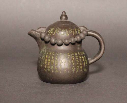 Blackish brown teapot with a gourd shaped body covered with incised Chinese characters and geometric lines  accented with yellow and circular beads hanging around the neck.