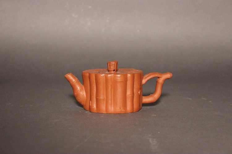 Light orangish brown teapot with a straight-sided body resembling a standing bunch of bamboo reeds of various thicknesses and a flat top. The lid is flat, and the spout and handle resemble bamboo reeds.