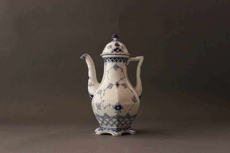 Tall white coffeepot with a bulbous body that tapers to a narrow neck featuring blue decorations in various patterns with central delicate floral motif, a long curved spout and a round domes lid with round finial.