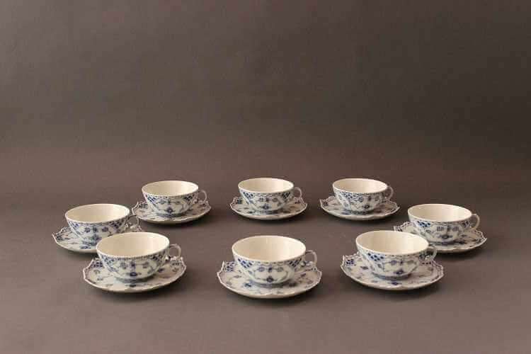 Eight white cups with delicate c-scroll handles and saucers, all having blue decoration all over in various patterns with central delicate floral motif.
