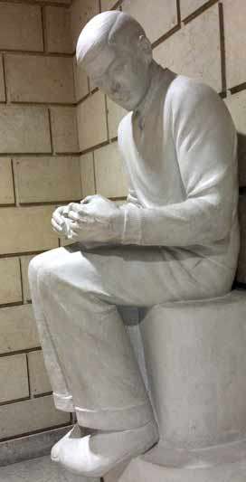 Sculpture of a seated boy reading a book on his lap looking slightly to his left.