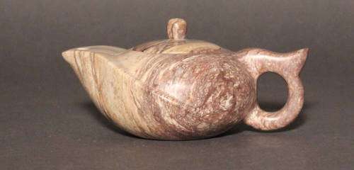 Stone teapot with small pale yellow brown round body carved into a curving pointed form featuring white veins that spread into purplish brown and a spout at the end point of the body.