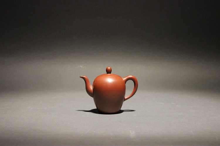 Small plain brick red egg-shaped teapot with flat bottom, s-curve spout and ear-shaped handle.