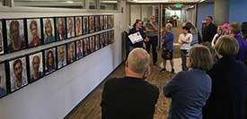 People viewing a collection of face paintings displayed in two rows.