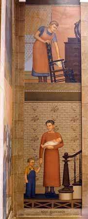 Tall mural showing two women on two levels of an indoor house. On the upper level, a woman in a blue short-sleeved gown and brown apron cleans a chair with a white cloth by a dark brown dresser pressed against a peach wall with a large window with curtains partially covering it from the top. On the lower level, a woman in a copper-colored gown standing by a dark brown staircase holds a baby wrapped in white cloth in one arm while holding the hand of a kid in blue overalls with the other arm and looking at h