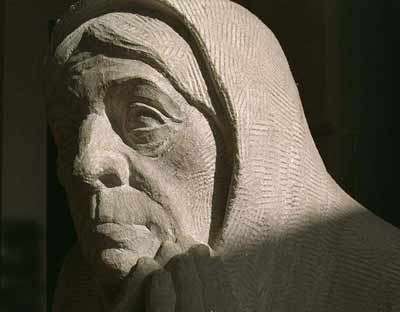 Sculpture of a woman praying while looking up in creme and black shadow.