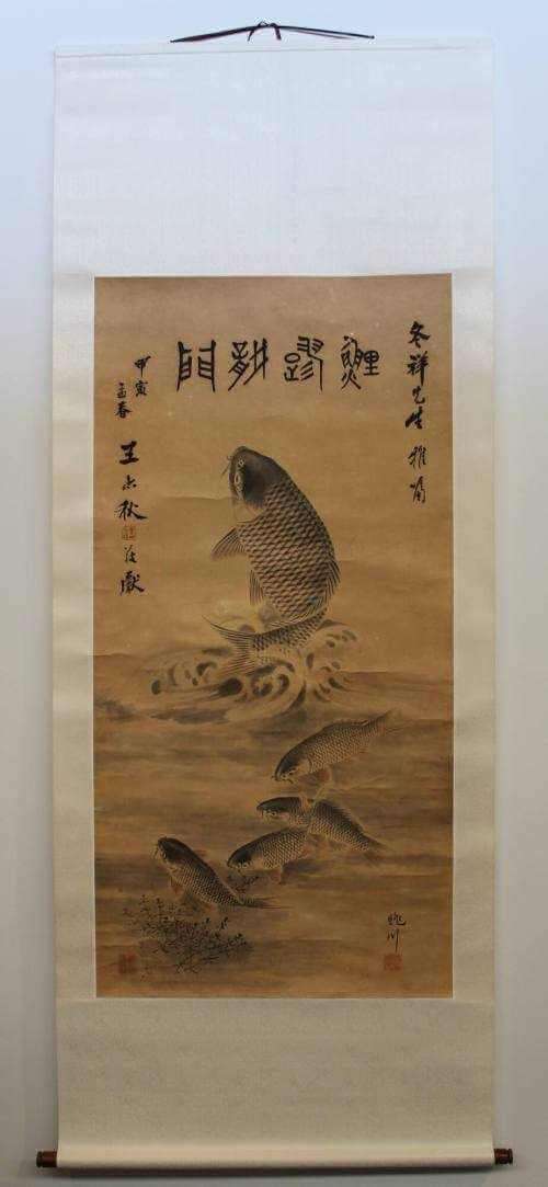 Hanging scroll showing large central koi fish twisted and jumping out of the water with pale blue waves below, four smaller koi swimming below, with some sea vegetation, 4 large central Chinese characters at top with vertical rows of calligraphy on each side.